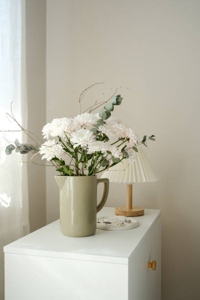 istock An elegant flowers display in arranged beautifully in a minimalistic vase that sits gracefully on a white surface with lamp, plate with accessories. 2203094283
