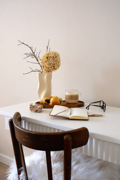 istock A cozy, minimalistic workspace with charming ceramic vase, dry branches flowers ,notebooks, glasses coffee and croissants on wooden stand. 2203094651
