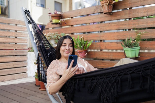 istock Woman relaxing on terrace hammock with smartphone 2203105528