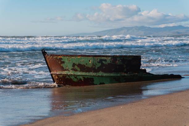 istock Rusted boat on sandy beach with waves and mountains. 2203107313