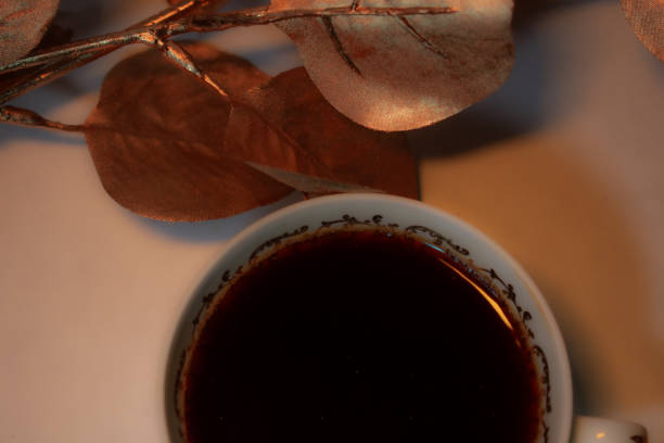 Istanbul, Turkey-June 20, 2022: Turkish coffee with plenty of foam in a white cup on mixed sheet music. Around the coffee are orange tulips and branches of white flowers. At the bottom of the coffee cup is an iron plate with a cream color vintage pattern. Shot with Canon EOS R5.