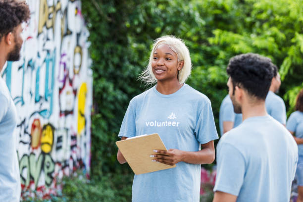 istock Young Female Volunteer Holding Clipboard, Discussing with Team 2203108599