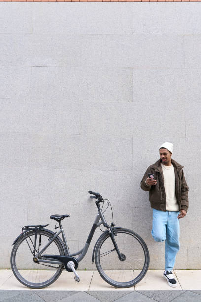 istock Stylish man leaning against wall using smartphone next to his bicycle 2203111246