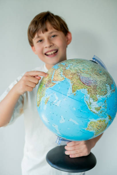 istock Little cute boy is looking at the globe with small airplane in his hands. 2203121384
