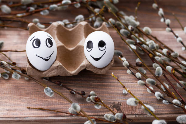 istock two white eggs with doodle cheerful faces and willow branches on wooden background 2203121779