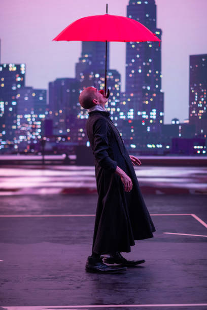 istock Mysterious Clown Performer with Red Umbrella in Urban Nightscape. 2203129119