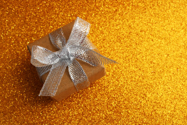 Gift box with silver glitter ribbon bow on a gold background