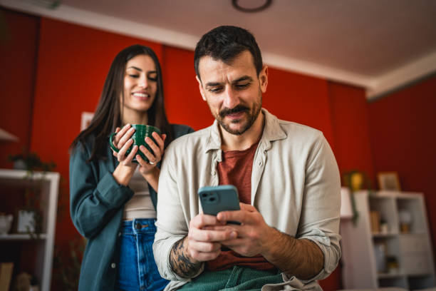 istock man use mobile phone while woman stand with cup of coffee behind him 2203135455