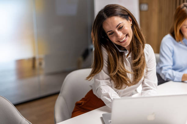 istock Businesswoman smiling while talking on phone and working on laptop 2203138081