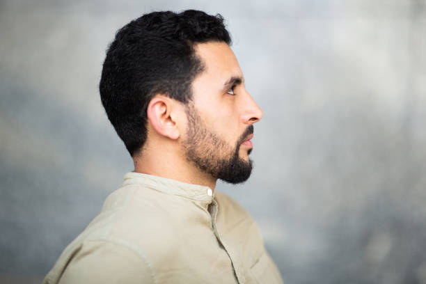 Profile portrait of young North African guy with serious expression against grey background