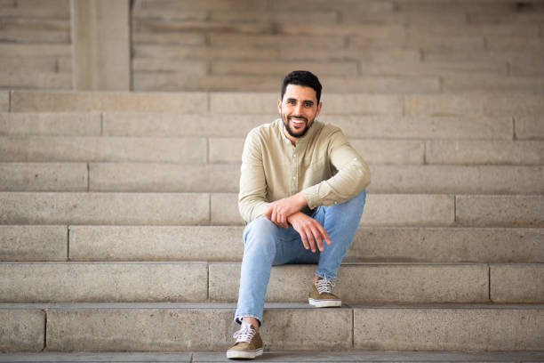 istock Handsome young arab man sitting on steps and smiling 2203139507