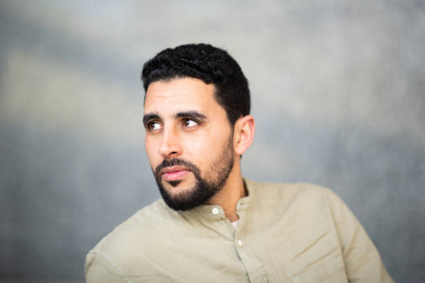 Close up portrait of young arabic man looking away  with serious expression against grey background
