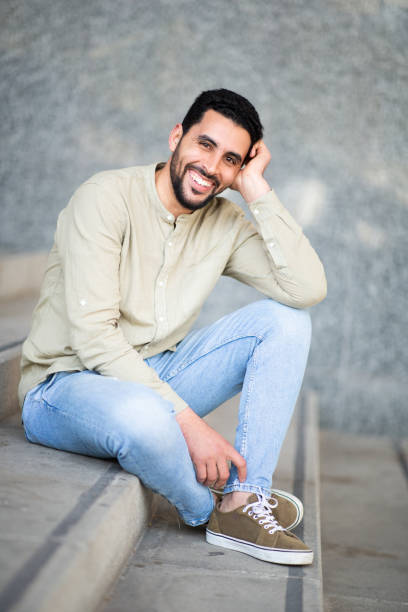 istock Portrait of smiling young arabic man sitting on steps 2203139568