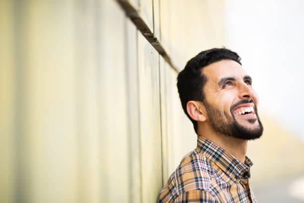 istock Handsome young arab man leaning to a wall looking away and smiling 2203139695