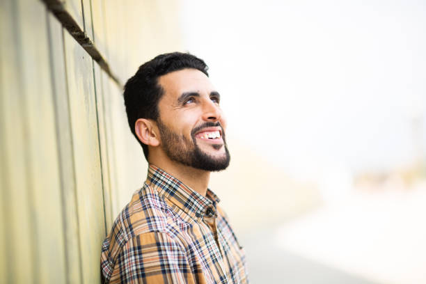 istock Happy young arabic guy looking away and smiling leaning to a wall 2203139750