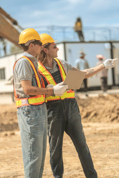 istock Two construction workers in hard hats and reflective vests discussing blueprints at an industrial site, emphasizing collaboration, planning, and safety in civil engineering projects. 2203141262