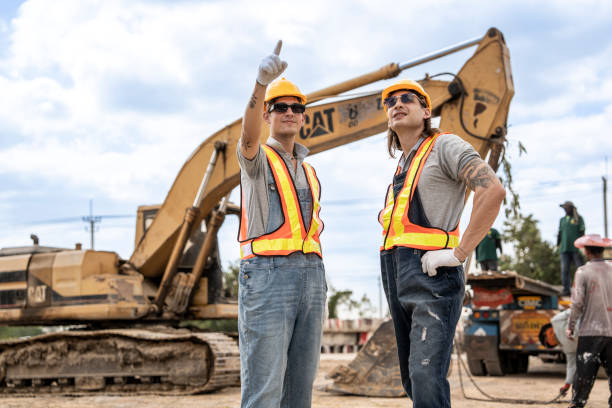 istock Construction workers in hard hats and reflective vests shaking hands, standing at a busy construction site with an excavator in the background, symbolizing successful teamwork. 2203141783