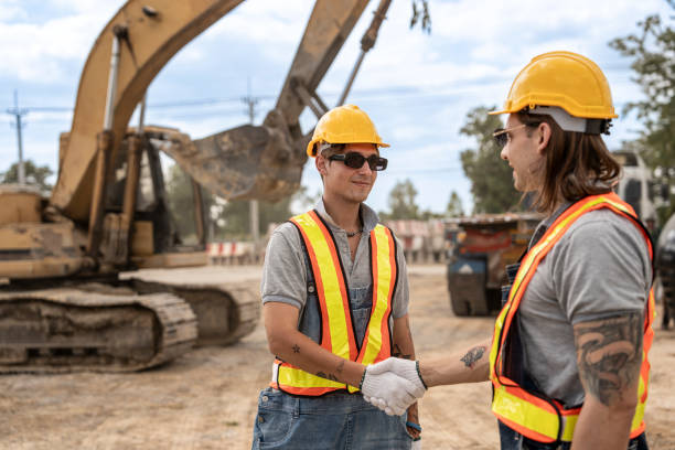 istock Two professional builders shaking hands in front of an excavator at a construction site, highlighting teamwork, industrial progress, and workplace collaboration. 2203142021
