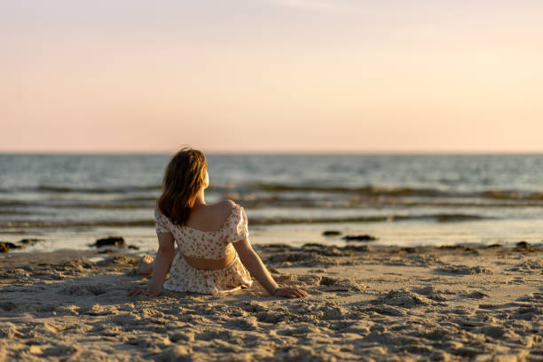 Woman relaxing on a sandy beach watching the sunset over the ocean while enjoying a peaceful evening