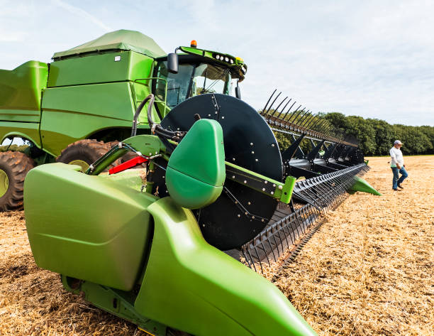 A farm worker inspects a large green combine harvester in a field. The machinery, with its massive tires and cutting blades, is essential for efficient harvesting. The image highlights modern agricultural practices and the importance of advanced farming equipment.