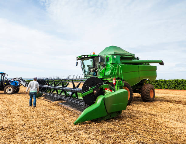 A farm worker inspects a large green combine harvester in a field. The machinery, with its massive tires and cutting blades, is essential for efficient harvesting. The image highlights modern agricultural practices and the importance of advanced farming equipment.