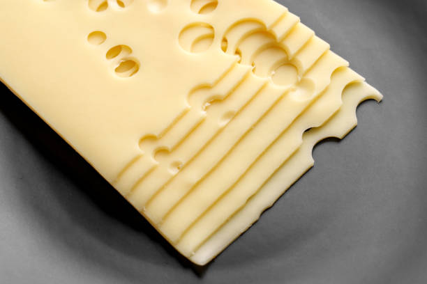 Swiss Emmental cheese slices on black kitchen ceramic plate close up.