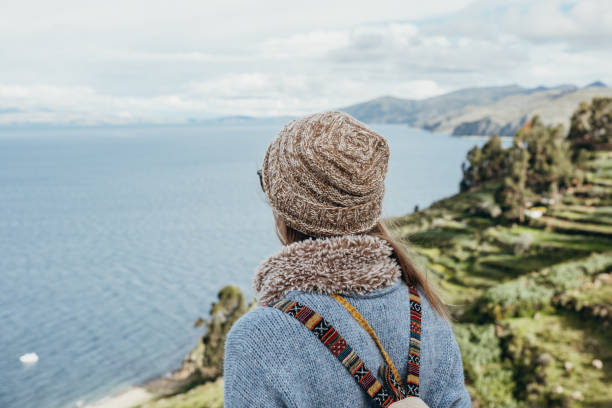 Woman in warm attire viewing ocean horizon from hilltop. Person with backpack exploring nature. Traveling and sightseeing in beautiful landscapes.