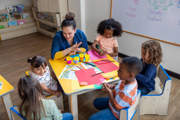istock Happy preschool teacher doing crafts in class with a group of young students 2203154701