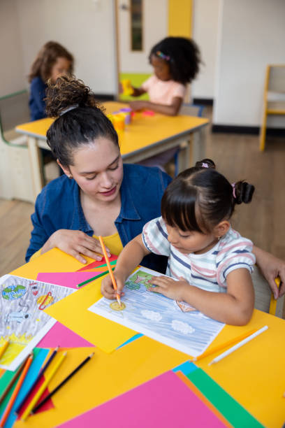 istock Preschool teacher supervising a girl while she is coloring in art class 2203154708