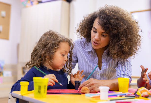 istock Happy kindergarten teacher supervising a schoolboy coloring in class 2203154721