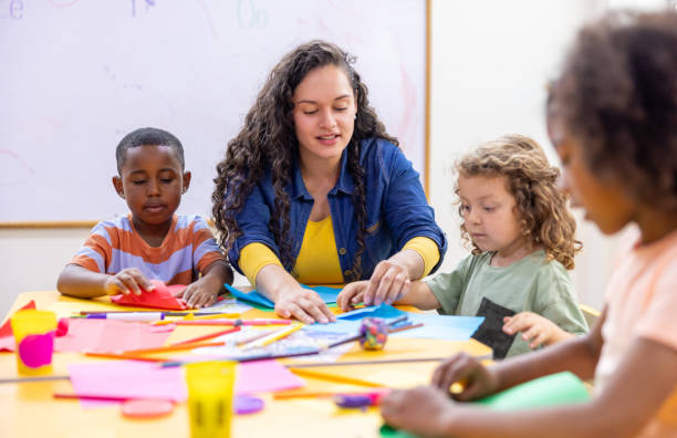 Happy Latin American preschool teacher helping children while doing crafts in class - education concepts