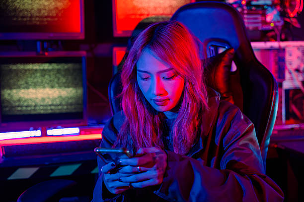istock Woman hacker. Asian woman wearing hood working at computer and mobile phone typing coding hacking programming system. Hacker browsing internet uses malware with smartphone to hack password 2203157054