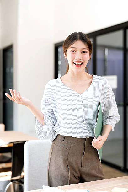 istock Beautiful young woman standing in office, smiling to the camera while presenting with hand 2203161120