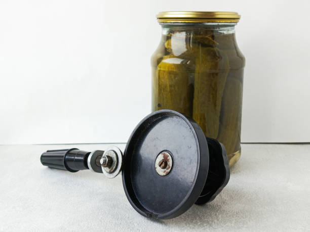 istock Seaming machine key and a jar with lightly salted cucumbers on the table. Recipe for crispy pickles with dill umbrellas and grape leaves. Brine. 2203172133