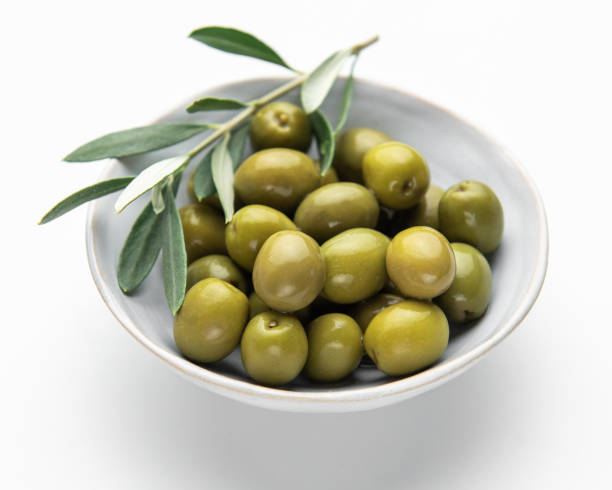 istock Green olives with olive branch resting in a bowl on white background 2203174483