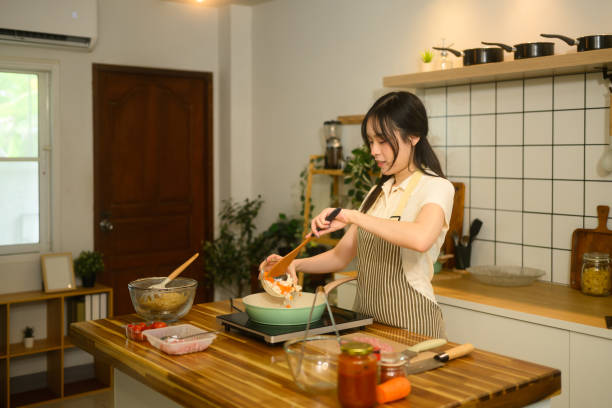 istock Young woman adding ingredients into a pan, preparing spaghetti in a modern kitchen 2203185911