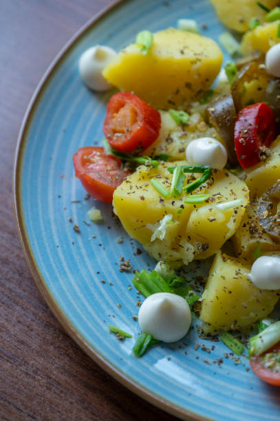 Freshly boiled potatoes, lightly seasoned and adorned with vibrant cherry tomatoes and chopped spring onions, create a colorful and appetizing dish perfect for any setting.