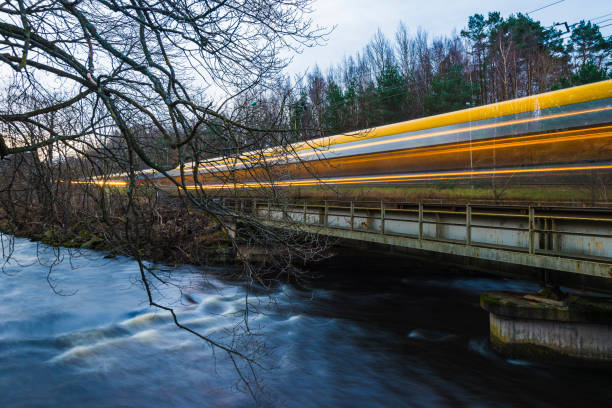 A train moves swiftly over a bridge spanning a river in Sweden as twilight settles.