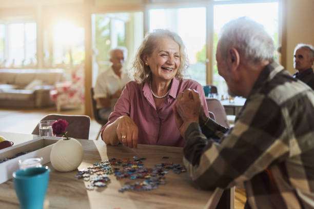 istock Happy mature couple talking while making jigsaw puzzle at nursing home. 2203188128