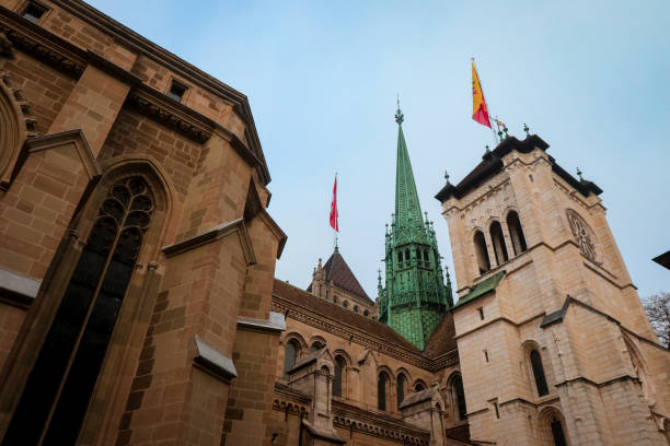 Low angle view of Nikolaikirche Villach church steeple spire illuminated by sunlight in contrast to gray cloud sky.