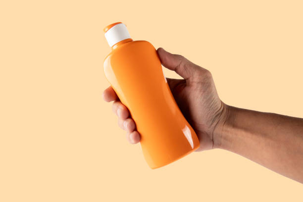 istock Hand holding a sun screen bottle isolated on light orange background 2203194019