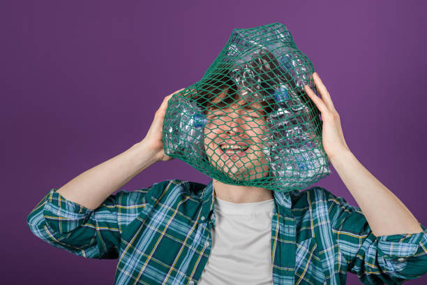 istock Young activist dons a recycling net filled with plastic bottles on his head, offering a poignant representation of the worldwide plastic pollution problem 2203195149