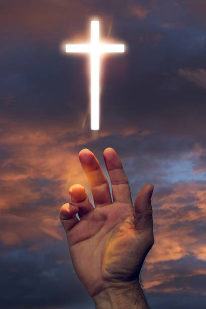 istock Hand Reaching for Glowing Cross in Sky 2203195253