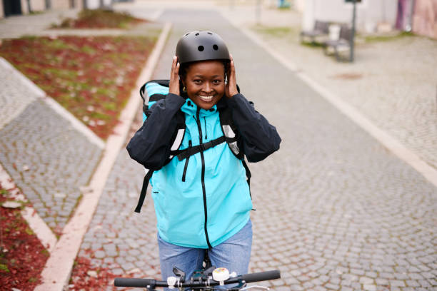 istock Smiling delivery woman adjusting her helmet while riding a bicycle 2203197463
