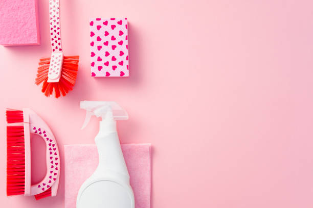 istock Cleaning services tools and supplies with heart patterns and white spray bottle on pink background. Flat lay, top view. 2203202368