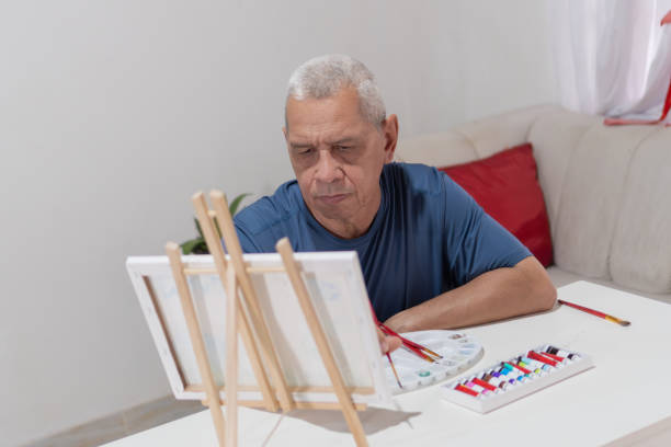 istock Senior hispanic man painting on canvas at home using an easel 2203204567