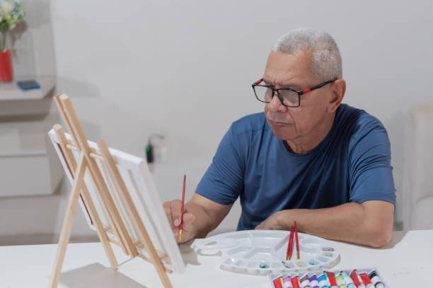 istock Senior adult artist painting on canvas at home using an easel 2203204607