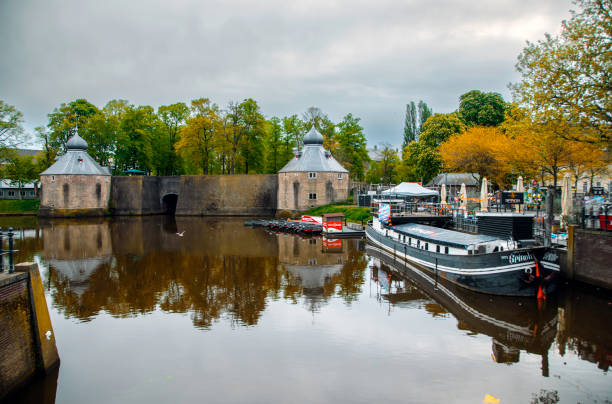 This historic Spanjaardsgat (Spanish Gate) in Breda, Netherlands, is a striking remnant of the city's medieval defense system. The image showcases one of the two heptagonal towers, part of Breda Castle and the former city fortifications, including the Granaattoren. The calm canal water reflects the imposing stone walls, creating a serene yet moody atmosphere. Located in the province of Brabant, Spanjaardsgat is steeped in history, famously linked to the capture of Breda in 1590 during the Eighty Years' War. The surrounding lush trees and an anchored boat add to the charm of this picturesque heritage site