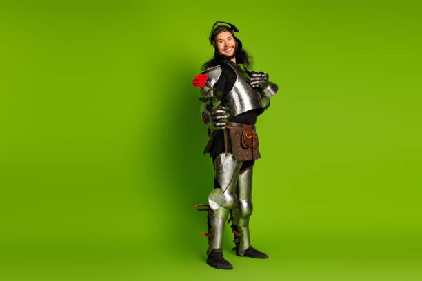 istock Young medieval knight holding a rose, standing amidst a vibrant green background wearing full steel armor, symbolizing chivalry and romance 2203206021