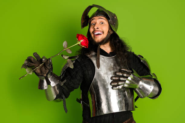 istock Young medieval knight in armor holding a rose on a green backdrop 2203206030